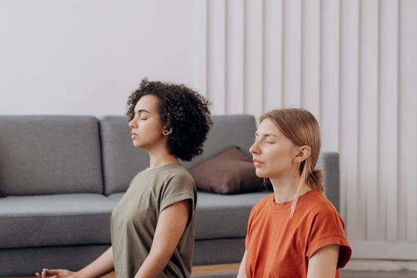 Woman sitting peacefully on a yoga mat in a bright, calm room.